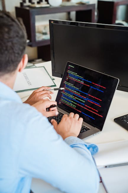 A close-up photograph of a laptop displaying a code editor on the left side with HTML and CSS code visible, alongside a large orange calculator application open on the right side of the screen. The la
